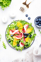 Gourmet salad with smoked duck, oranges, blueberries, arugula and lettuce, white table background, top view