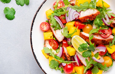 Grilled chicken salad with mango salsa, tomato, cilantro, red onion and lettuce in mexican style, gray table background, top view close-up