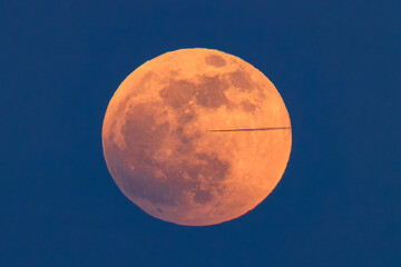 A jet and its contrail crosses the full moon on the night of the blood moon total eclipse.