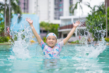 Asian child happy smile in swimming pool or kid girl wear swimsuit and fun splashing water in waterpark or person learning swim to sports exercise on summer school or holiday vacation travel at hotel