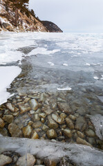 Winter landscape of frozen Baikal Lake with transparent ice near the shore on cold day in January. Stones at the bottom of the lake are visible through the clear ice. Winter travel and outdoors