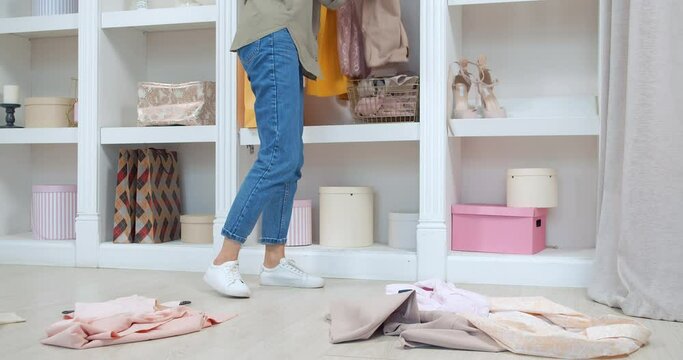 Young woman picking up clothes scattered on the floor and putting them in a closet in a dressing room or store