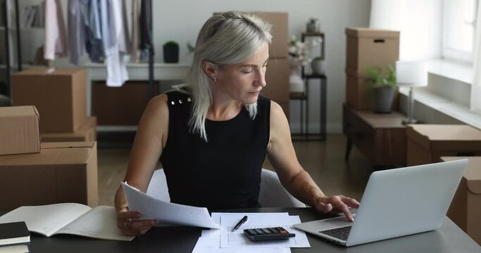 Mature woman fashion designer do accountancy job sit at desk, calculates expenses and incomes, lead small business accounting looks focused working in office. Entrepreneurship, financial management