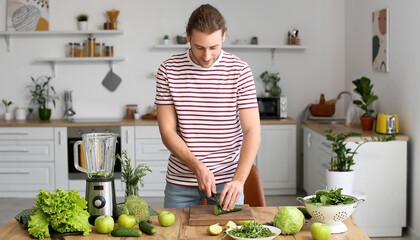 Young man with modern blender making green smoothie in kitchen at home - Powered by Adobe