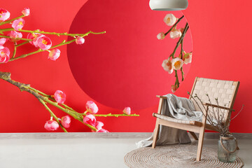 Stylish armchair near red wall with blooming Chinese plum branches in room