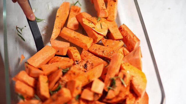 Cook stirs the baked sweet potato with rosemary in a deep dish with a spatula