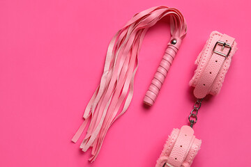 Handcuffs and whip from sex shop on pink background