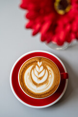 Cup of red latte coffee, top view with blurred red flowers