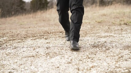 Walking in black cowboy boots over gravel and dirt in the country.