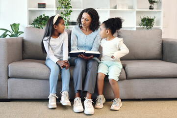 Senior family reading books to children, teaching and learning bible story, questions and education in living room. Grandmother and kids on sofa with storytelling or holy religion, knowledge and help © Allistair F/peopleimages.com