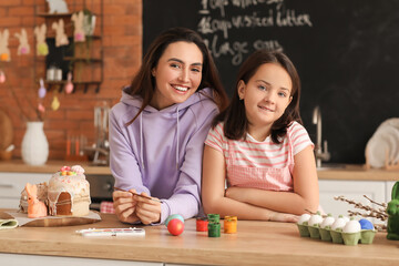 Fototapeta premium Little girl and her mother painting Easter eggs at table in kitchen