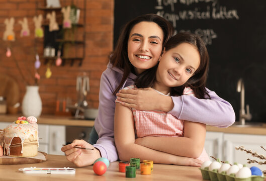 Little girl and her mother painting Easter eggs at table in kitchen