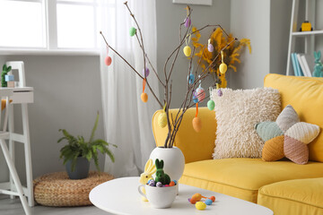 Vase with tree branches, Easter eggs, rabbits and cup on table in living room
