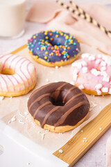 Board with different delicious donuts on white table