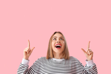 Young woman in striped sweatshirt pointing at something on pink background