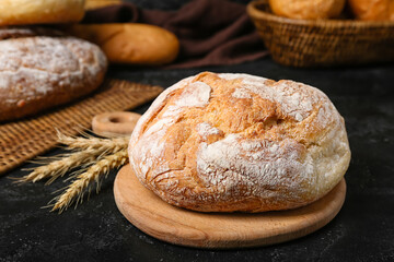 Cutting board with loaf of fresh bread and wheat ears on black table