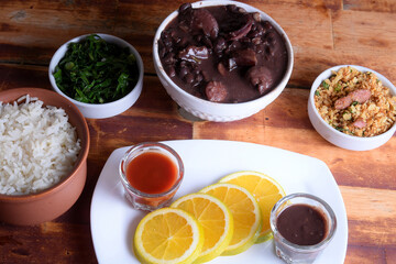 traditional Brazilian food feijoada with beans, pork, bacon, sausage with cabbage, rice, salad, spices and pepper. rustic kitchen