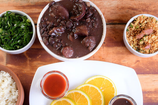 traditional Brazilian food feijoada with beans, pork, bacon, sausage with cabbage, rice, salad, spices and pepper. rustic kitchen