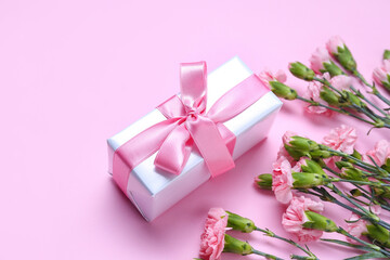 Gift box and beautiful carnation flowers on pink background. Women's Day celebration