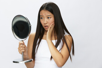 Asian woman with mirror in hand facial skin problems, acne and inflammation, red rash and...