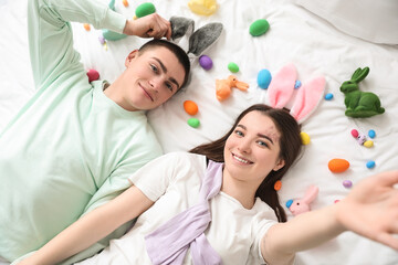 Young couple in bunny ears with Easter eggs and rabbits lying on bed, top view