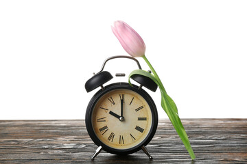 Alarm clock and beautiful tulip flower on wooden table against white background