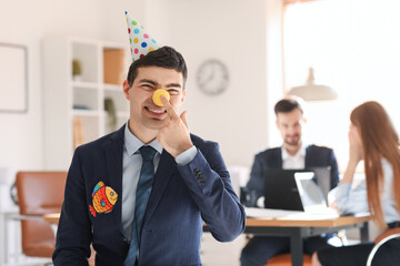 Young man with party hat and clown nose in office. April Fools' Day celebration