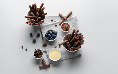 Composition with delicious chocolate wafer rolls, blueberries, condensed milk and coffee beans on grey background