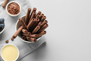Bowl with delicious chocolate wafer rolls and condensed milk on grey background