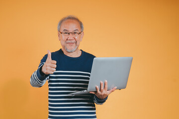 Asian senior man using laptop computer for working after retirement on the yellow background.