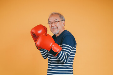 Asian senior man with boxing glove on the yellow background.