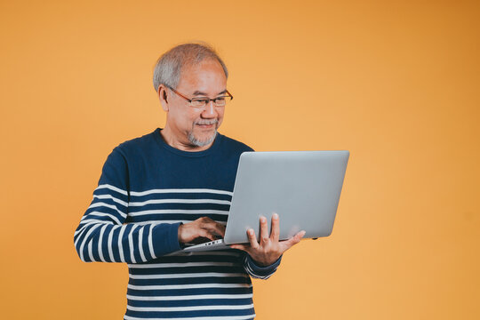 Asian Senior Man Using Laptop Computer For Working After Retirement On The Yellow Background.