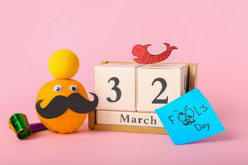 Composition with cube calendar, funny orange and decor on pink background. April Fool's Day celebration