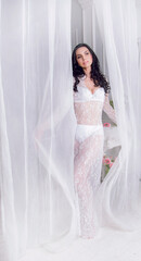 A young brunette dressed as a Bride in lingerie and a boudoir dress poses surrounded by a stunning floral décor.