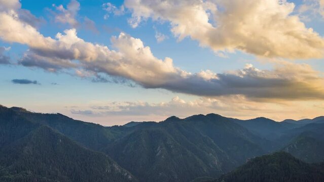 Clouds float across the blue sky with sunlight over the valley of the Rhodope Mountains with spruce forests