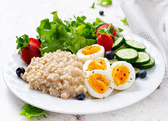 Breakfast oatmeal porridge with boiled eggs, cucumber and strawberry. Healthy balanced food.