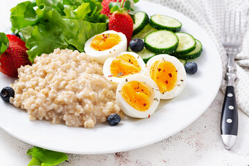 Breakfast oatmeal porridge with boiled eggs, cucumber and strawberry. Healthy balanced food.