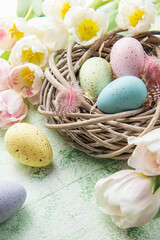 Nest with Easter eggs painted pastel colors on a green wooden background.
