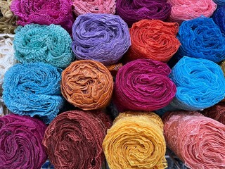 Many rolls of colorful lace fabric with beautiful floral pattern on a shelf in knitting store.