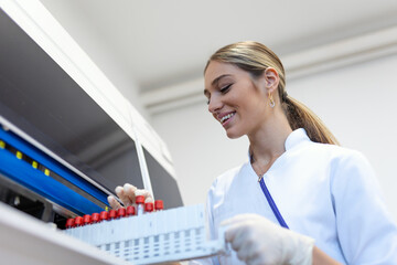 Portrait of a young female laboratory assistant making analysis with test tubes and analyzer machines sitting at the modern laboratory