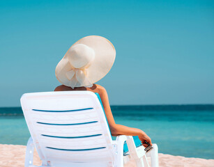 Fototapeta na wymiar Woman lies on a sunbed in a large white hat on the background of the sea, photo 3