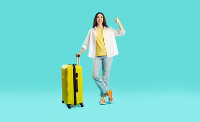 Passenger traveling abroad to travel on weekends getaway. Traveler tourist woman in summer casual clothes with suitcase showing thumb up isolated on light blue background. Air flight journey concept