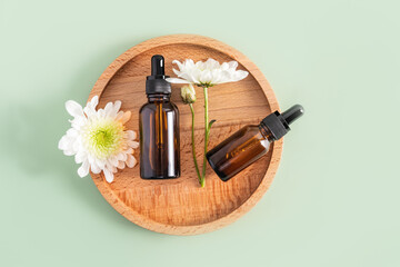 Two cosmetic bottles with an organic natural self-care pipette lie on a round wooden tray with...