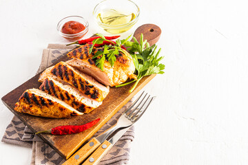 a wooden cutting board with slices of delicious juicy grilled chicken tomb cut on it. tomato sauce in a bowl. white background. space for text.
