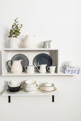 various cookware on open white shelves on a white stylish wall. vertical view. decorative items in the interior of the kitchen.