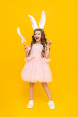 Easter children's holiday. A teenage girl in a lush dress rejoices in spring. The child is wearing long rabbit ears. A beautiful little girl with long hair, full-length on a yellow isolated background