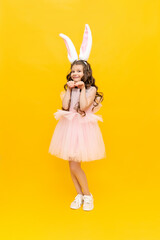 Festive Easter. A teenage girl in a fluffy dress and with rabbit ears is smiling broadly. A beautiful little girl in a rabbit costume on a yellow isolated background, full-length.