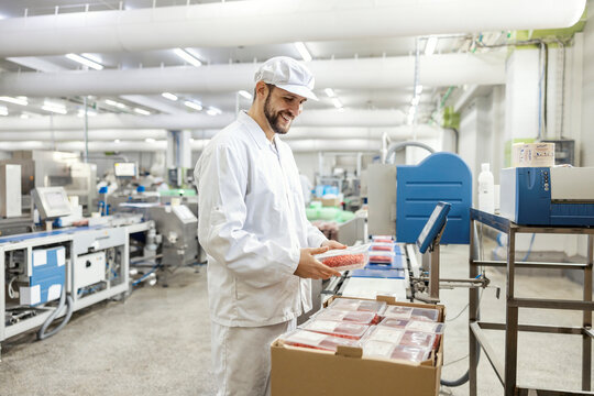 A happy meat industry worker is packing minced meat into a box and getting ready to deliver it.