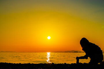 Naklejka na ściany i meble Silhouette of a woman piling stones against the setting sun