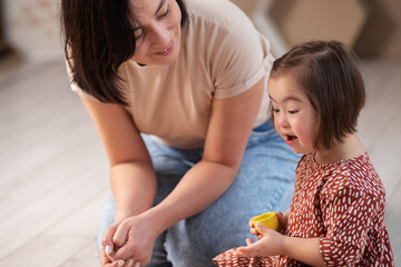 cute happy girl with down syndrome at home with mom playing with toys